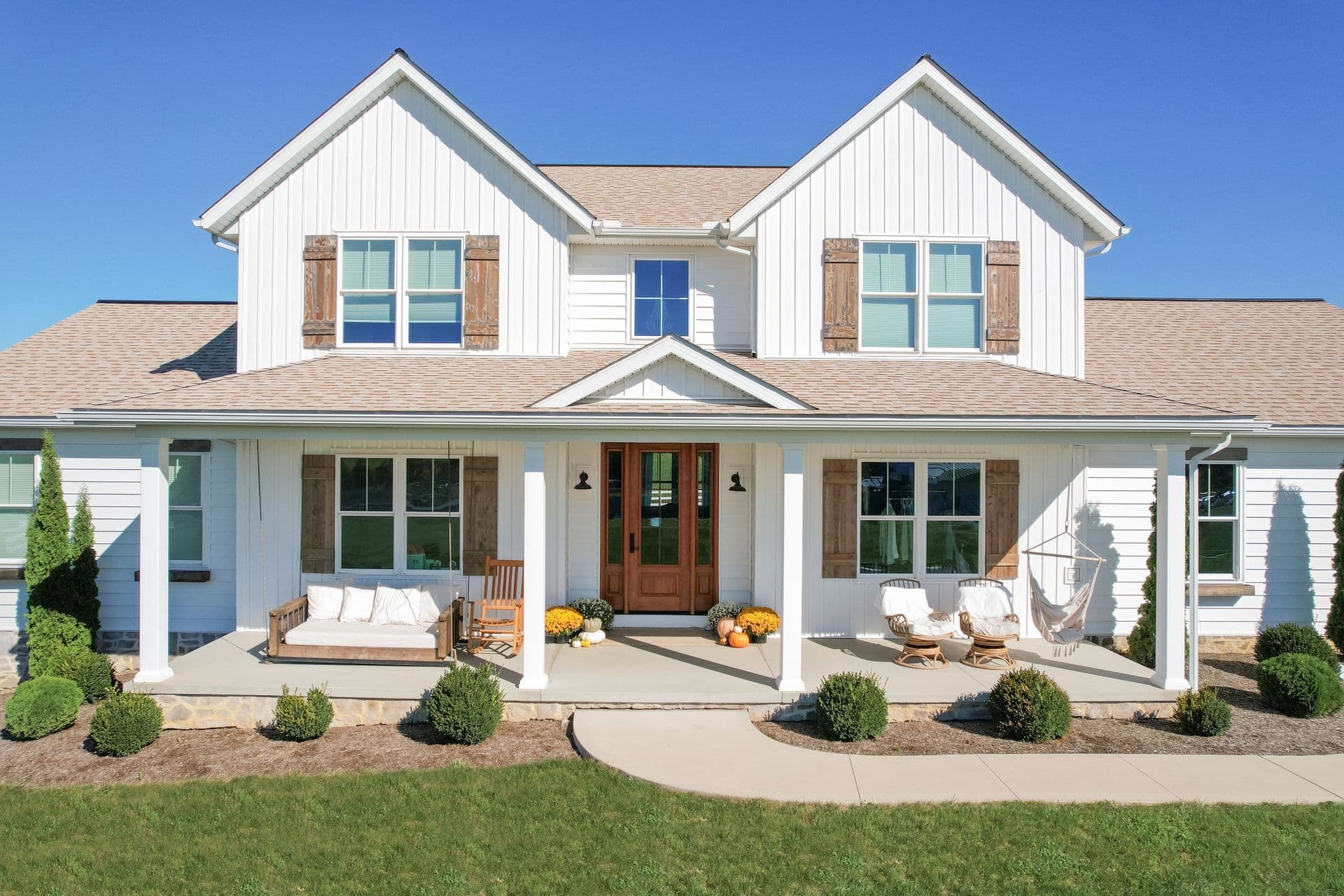 A large white house with horizontal and vertical shiplap siding, new replacement windows, and a brown front door with door lite.